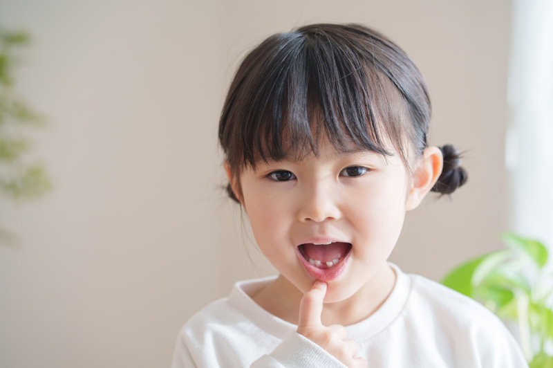 下の前歯の乳歯が抜けたところを指さす女の子