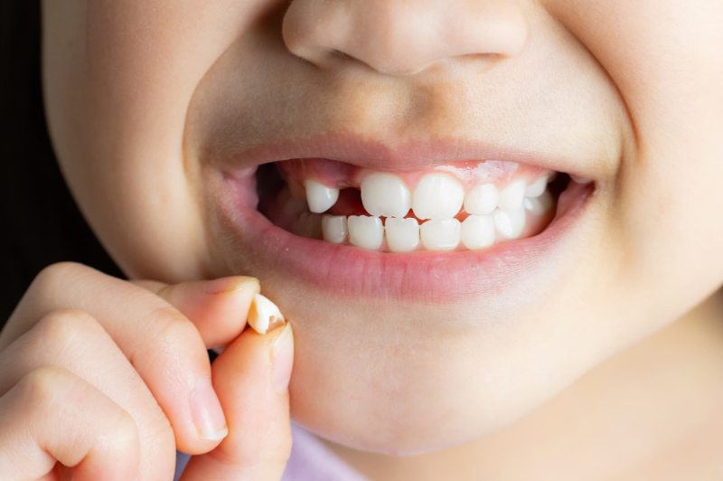 抜けた乳歯を持って微笑む子供の口元