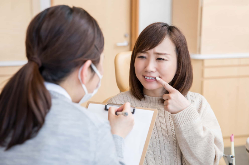 歯の矯正後に後戻りが起こって歯科医に相談する女性