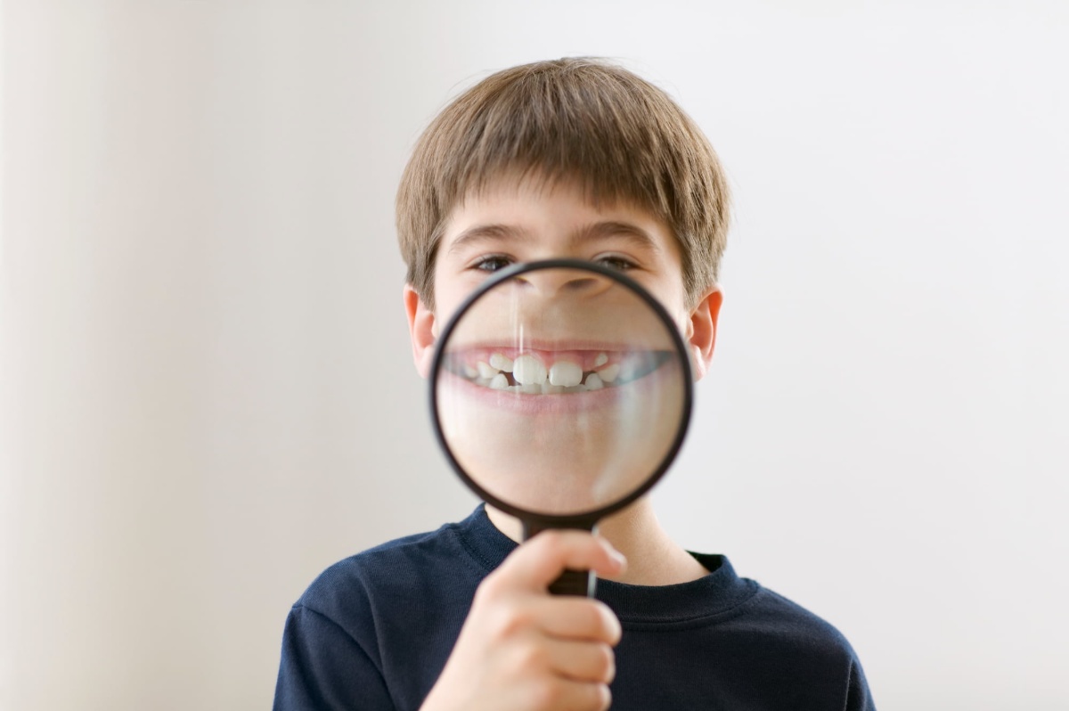 虫眼鏡で自分の出っ歯を拡大してみせる子ども